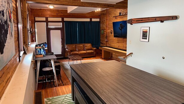 A compact living space with a wooden ceiling, a sofa, a dining table, and a TV mounted on the wall. - The Office at North Creek All Season Rental (North Creek)