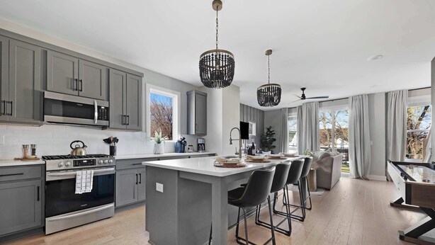 A modern kitchen with grey cabinets, stainless steel appliances, and a central island with bar stools.