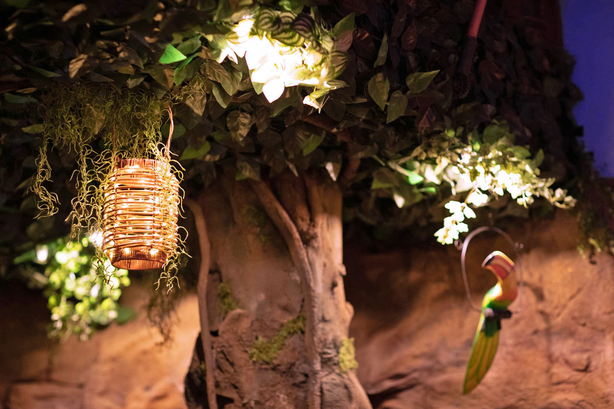 A hanging lantern and a bird sculpture in a botanical setting.