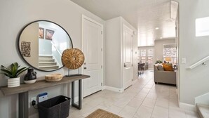 A modern hallway with a round mirror, a console table with decorative items, and a staircase leading to a living area. - Lazy River Retreat, LOADED WITH EXTRAS! (Washington)