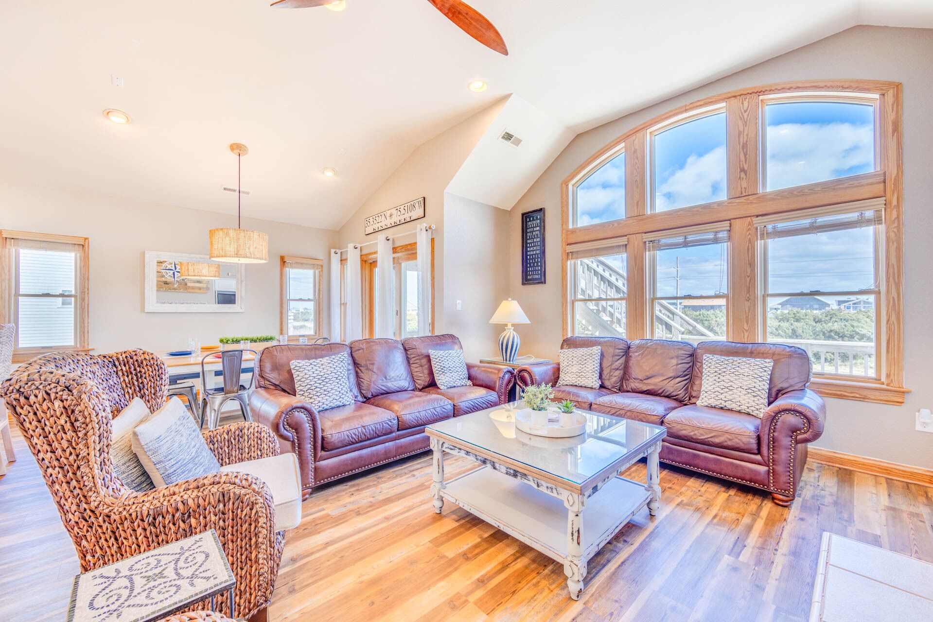A spacious living room with leather sofas, a glass coffee table, and a large window offering a view of the outdoors.