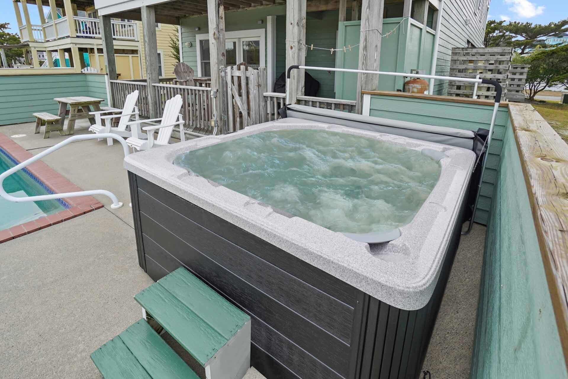 A hot tub with a wooden deck and a pool in the background.
