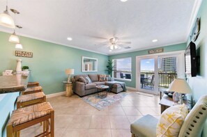 Relax in this open-plan living area with a sofa set, coffee table, and sliding glass door leading to a balcony with a scenic view.
