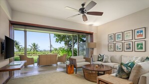 Amplia sala de estar con televisor grande, asientos cómodos, ventilador de techo y vistas al exterior.