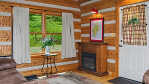 Interior de una cabaña de madera con chimenea, un mapa en la pared y una puerta con cortinas escocesas.
