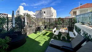 Eine Terrasse mit grünem Rasen, Sitzgelegenheiten im Freien und Blick auf umliegende Gebäude.