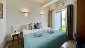 Ein Hotelzimmer mit einem großen Bett, zwei Wandleuchten, einem kleinen Nachttisch und Blick ins Freie durch eine Schiebetür.