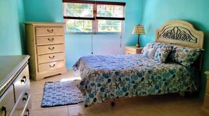 Un dormitorio con cama, cómoda, mesita de noche, lámpara y ventana con persianas.