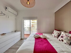 A modern bedroom with a large bed, a white dresser, and a hanging light fixture. - QUARTEIRA DESIGN by HOMING (Quarteira)