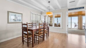A dining area with a wooden table and chairs, a pendant light, and a view of the lake through large windows. - Krusty Krab! Lakefront Getaway, Walk to Downtown! (Port Sanilac)