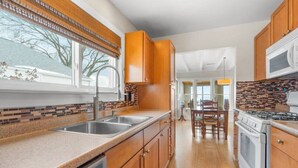 A kitchen with wooden cabinets, a granite countertop, a sink, a stove, and a microwave. - Krusty Krab! Lakefront Getaway, Walk to Downtown! (Port Sanilac)