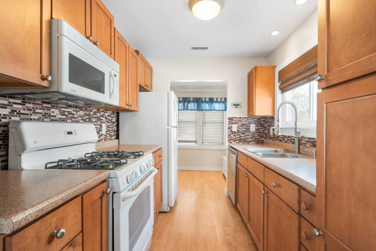 A compact kitchen with wooden cabinets, a microwave, stove, refrigerator, and a tiled backsplash.