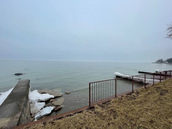 A waterfront view with a concrete barrier, metal railing, and a grassy area.