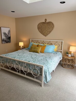 Quarto com uma cama, duas mesas de cabeceira, um coração decorativo na parede e uma planta emoldurada.