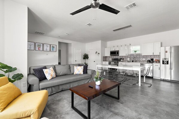 A modern living room with a grey sofa, yellow armchair, and a wooden coffee table. A ceiling fan is visible above.