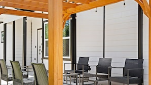 Ein Sitzbereich im Freien mit Korbstühlen und Tischen, einer Holzw pergola und großen Fenstern.