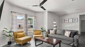 Ein modernes Wohnzimmer mit einer Couch, Sesseln, einem Couchtisch und einem Deckenventilator.