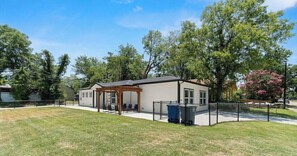 A single-story house with a covered patio, a fenced yard, and a trash bin.