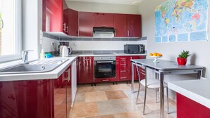 A modern kitchen with red cabinets, a stainless steel sink, a microwave, and a large world map on the wall. - La Pêcherie d'Utah - Charmante longère - Proche mer (Audouville-la-Hubert)