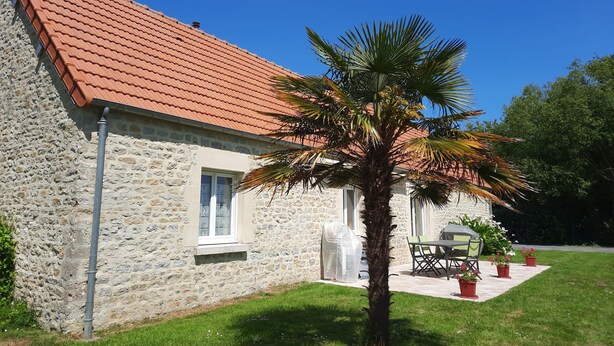 A stone building with a red-tiled roof, a palm tree, and outdoor seating. - La Pêcherie d'Utah - Charmante longère - Proche mer (Audouville-la-Hubert)