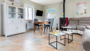 A dining area with a wooden table and chairs, a cabinet with glass doors, a television, and a poster on the wall. - La Pêcherie d'Utah - Charmante longère - Proche mer (Audouville-la-Hubert)