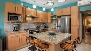 A modern kitchen with wooden cabinets, granite countertops, a central island with bar stools, stainless steel appliances, and pendant lighting.