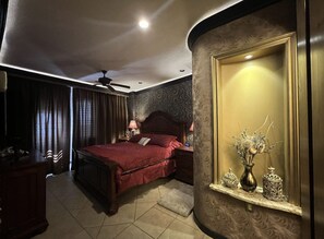 Een slaapkamer met een groot bed, nachtkastje, dressoir en spiegel, versierd met decoratieve voorwerpen.