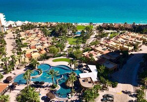 Luchtbeeld van een resort met meerdere gebouwen, een groot zwembad en een strand.