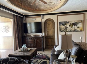 A living room with a flat-screen TV, a leather sofa, a coffee table, and a world map painting.