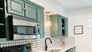 Una cocina con armarios color turquesa, una estufa negra, una encimera blanca y un salpicadero con estampado.