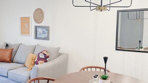 Un comedor con una mesa redonda de madera, cuatro sillas, una araña, un sofá con cojines y adornos en las paredes.