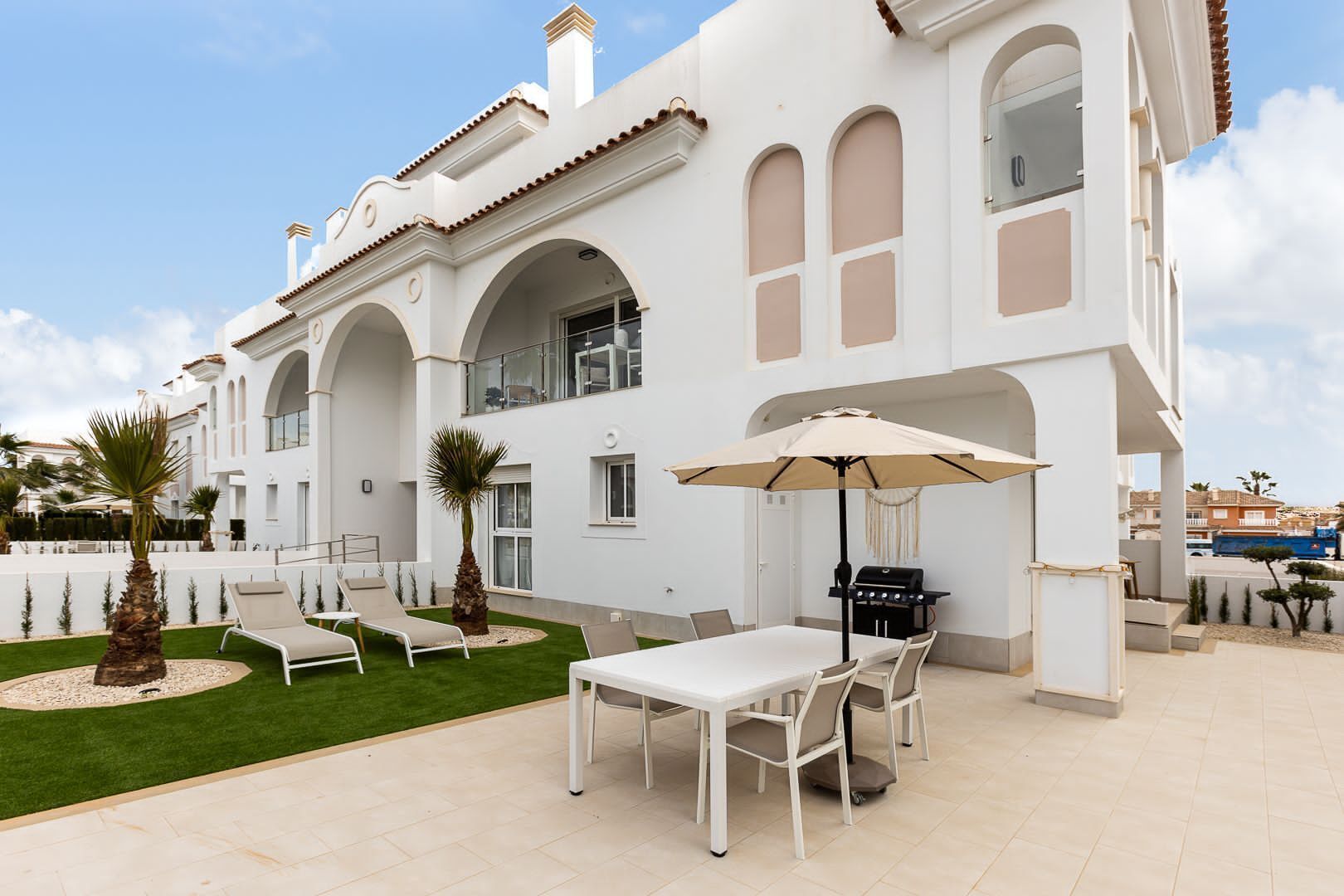 A white villa with a patio, outdoor seating, and a grill.