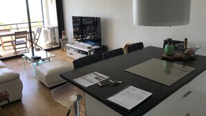 A modern living room with a large TV, dining area, and a glass coffee table. - APARTMENT FACING THE SEA, 20 metres from the beach (La Grande-Motte)