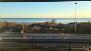 A view of the ocean from a window overlooking a road with a guardrail and sparse vegetation. - APARTMENT FACING THE SEA, 20 metres from the beach (La Grande-Motte)