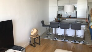 A modern kitchen with white cabinets, a central island with bar stools, and a built-in oven. - APARTMENT FACING THE SEA, 20 metres from the beach (La Grande-Motte)