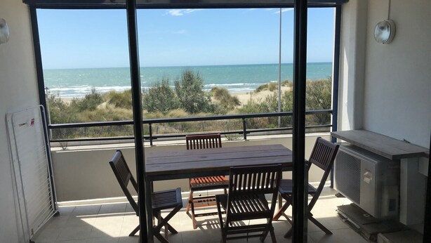 A balcony with a table and chairs, overlooking a beach and ocean. - APARTMENT FACING THE SEA, 20 metres from the beach (La Grande-Motte)