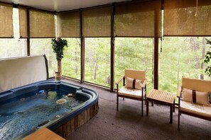 Relax in a serene space with a hot tub, two chairs, and a table, surrounded by a lush forest view.