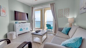 Un soggiorno con televisore, divano e tavolino. È presente un balcone con vista sull'oceano.