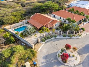 A residential property with a swimming pool, multiple houses with red-tiled roofs, and landscaped gardens.