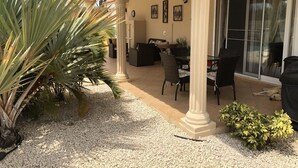 Un patio techado con un conjunto de asientos, plantas de palma y un perro acostado en el suelo.