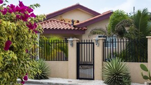 Una casa con techo de tejas, entrada protegida por un portón y varias plantas a su alrededor.