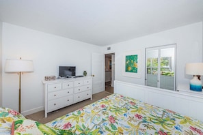 A bedroom with a bed, dresser, television, and artwork.