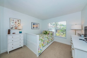 A bedroom with a bed, a dresser, a nightstand, a lamp, and a window with blinds.