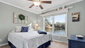 Une chambre à coucher avec un lit, un ventilateur de plafond, une fenêtre donnant sur un beau paysage et une commode.