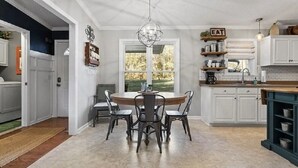 Une cuisine avec des meubles blancs, une table à manger en bois et un lustre.