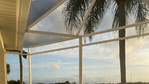 An outdoor patio with two white chairs, a pool, and a view of a lake. - 4-Bedroom Villa with Pool & Jacuzzi, Mangrove View (Port St. Lucie)