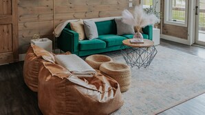 Een ruime woonkamer met een houten plafond, grote ramen, een groene bank en een plafondventilator.