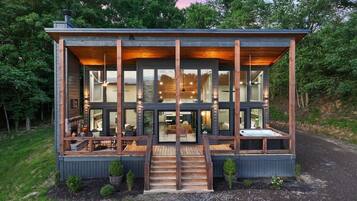 Une cabane moderne dotée d’une terrasse en bois, de grandes fenêtres et d’une cheminée.