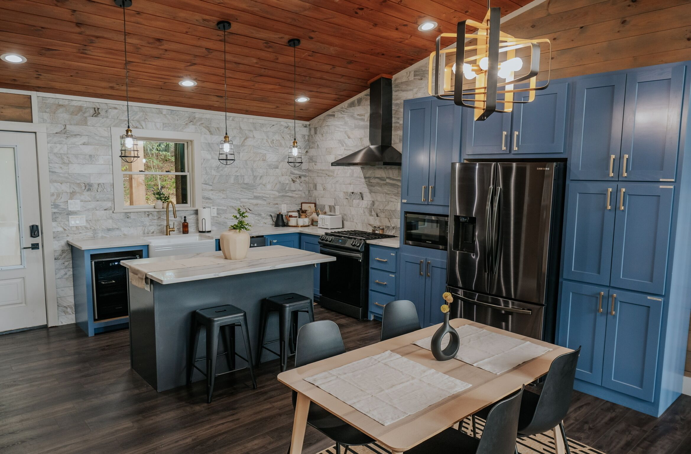 Une cuisine moderne avec des meubles bleus, un îlot central, des appareils en acier inoxydable et un plafond en bois.