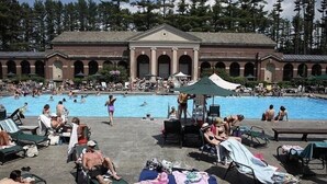 A pool area with lounge chairs and umbrellas, surrounded by a building with arched windows and a central entrance.
